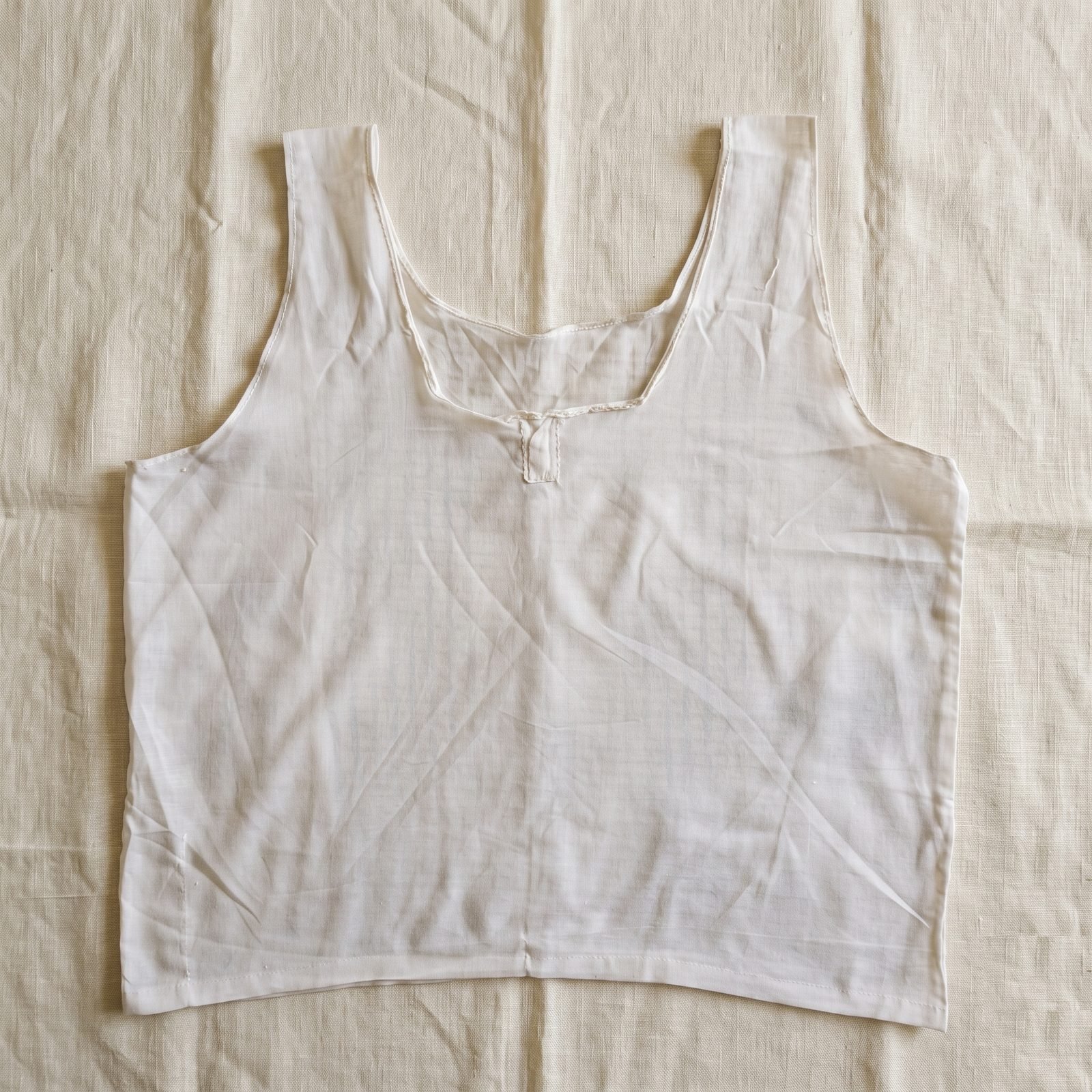 A sleeveless white Parsi Sadra laid flat, front view